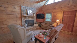 L’intérieur d’un chalet confortable, avec une cheminée, des canapés en cuir, un téléviseur et un plafond en bois.