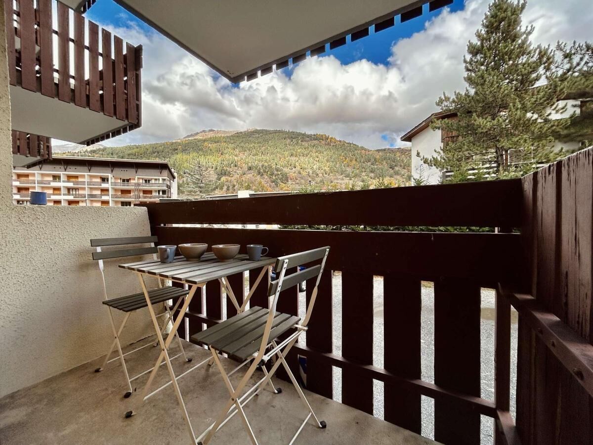 En balkon med bord og stole, udsigt til et bjerg, og et træværkshegn.