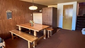A wooden dining table with benches, a hanging light fixture, and a small flower arrangement. - 100m from shops, 1st floor, balcony, tv, ski locker, 52m², Alpe d'Huez (L'Alpe d'Huez)