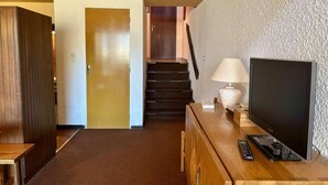 A hotel room with a wooden desk, a television, a lamp, and a staircase leading to another room. - 100m from shops, 1st floor, balcony, tv, ski locker, 52m², Alpe d'Huez (L'Alpe d'Huez)