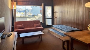 A hotel room with a sofa, a bed with a wooden frame, a small table, and a TV. - 100m from shops, 1st floor, balcony, tv, ski locker, 52m², Alpe d'Huez (L'Alpe d'Huez)