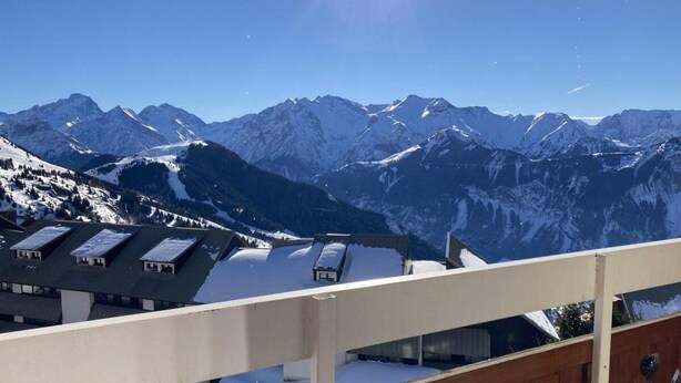 Vista de la montaña desde un balcón, con tejados nevados y una valla de madera.