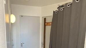 Un pasillo con piso de madera, una puerta blanca y una cortina gris.