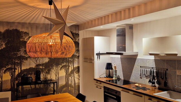 Une cuisine moderne avec un coin repas, agrémentée d’un luminaire suspendu original, d’une fresque murale et d’un îlot central.