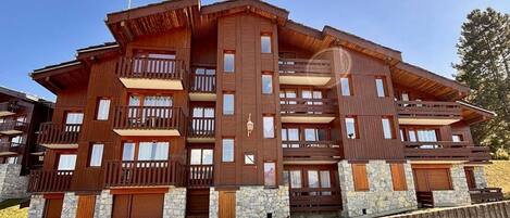A multi-story wooden building with balconies, stone accents, and a clear sky.