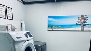 Una sala de bugaderia amb una rentadora, una assecadora i un cartell fixat a la paret amb vista a la platja.