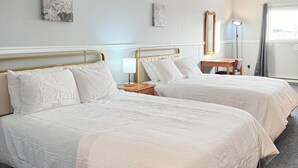 Habitació d'hotel amb dos llits, una taula de treball, una cadira, un mirall i una finestra amb cortines.
