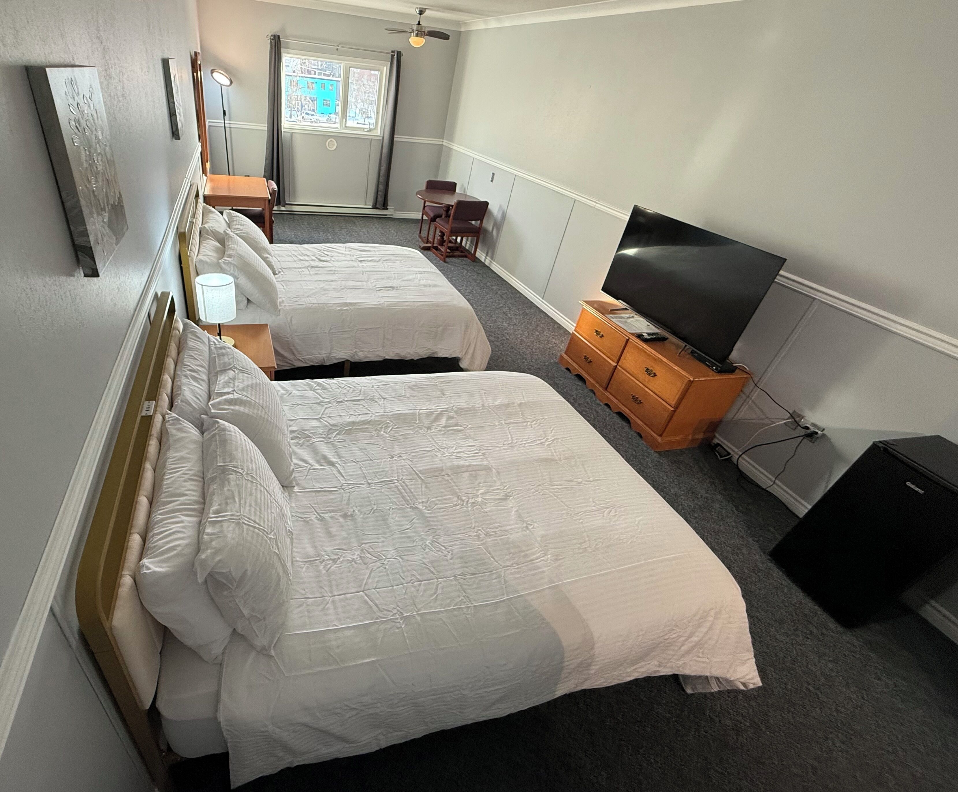 A hotel room with two beds, a TV, a dresser, and a window with curtains.