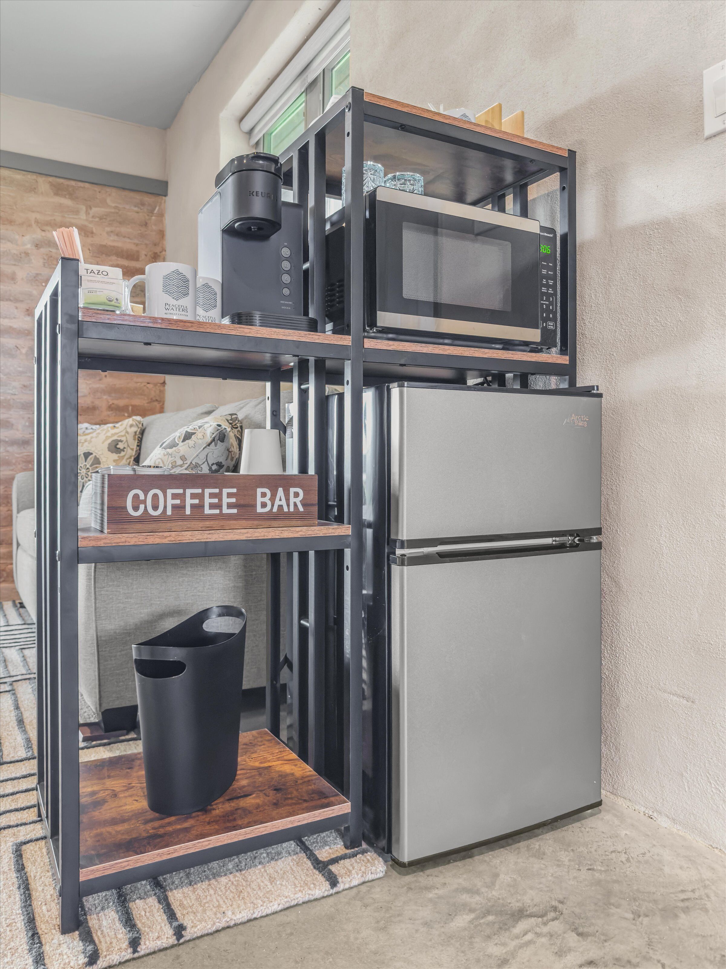 Een kitchenette met een koffiegedeelte, magnetron, koelkast en een prullenbak.
