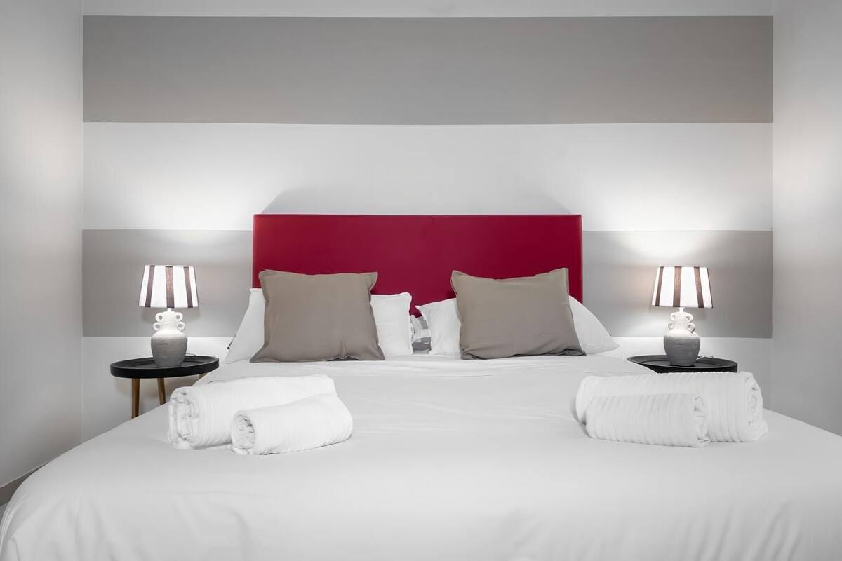 Une chambre d’hôtel avec un grand lit, deux tables de chevet avec des lampes et une tête de lit rouge.