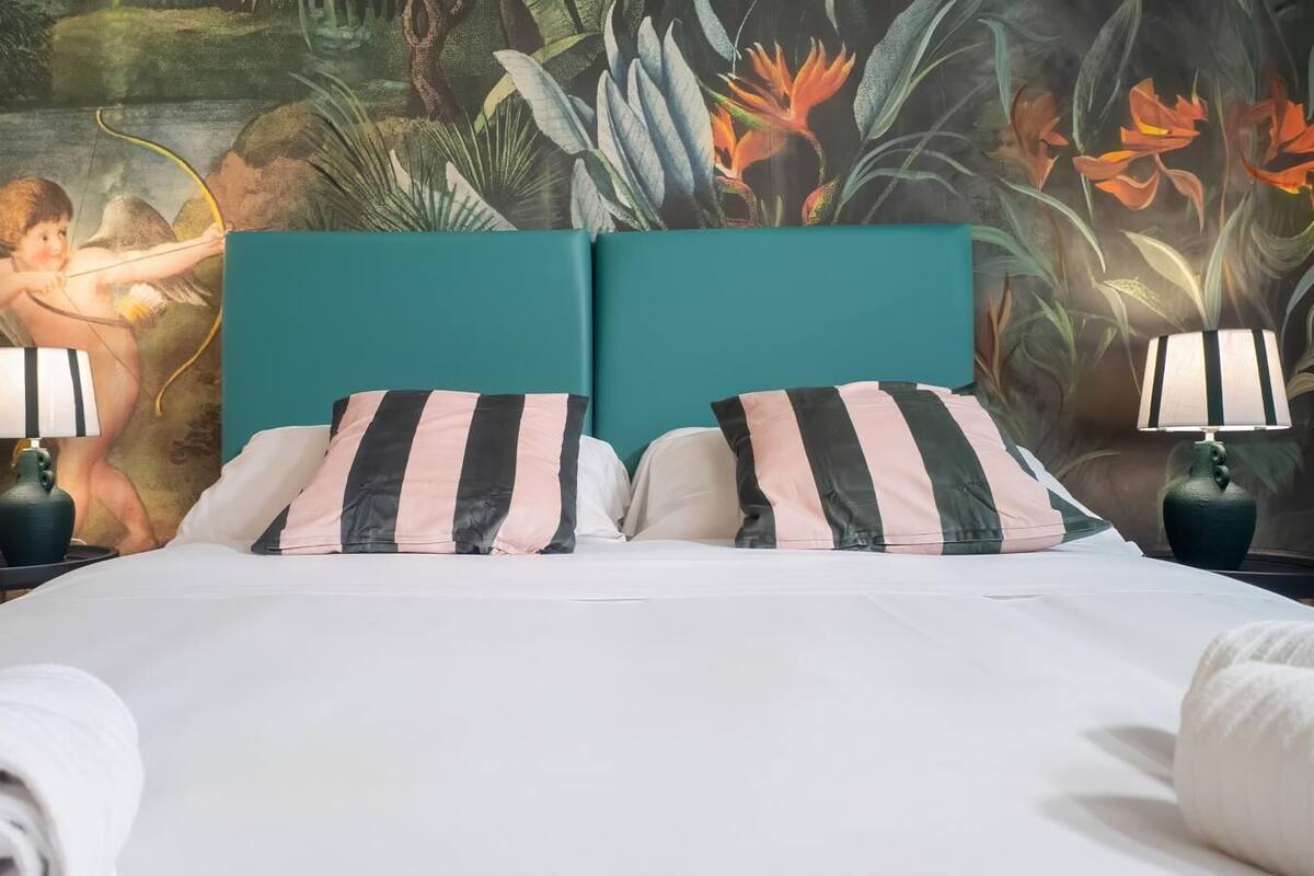 Un lit avec des oreillers à rayures, une tête de lit de couleur turquoise et deux lampes de chevet.