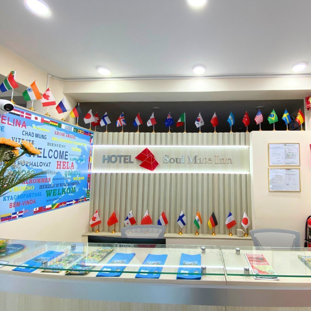 A hotel reception desk with a sign reading 'HOTEL Soul Mate Inn' and multiple national flags displayed above.