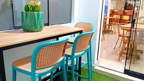 A dining area with a wooden table and turquoise chairs, a green vase with white flowers, and a view into a restaurant through a glass partition. - HOTEL SOUL MATE INN  (Lima)