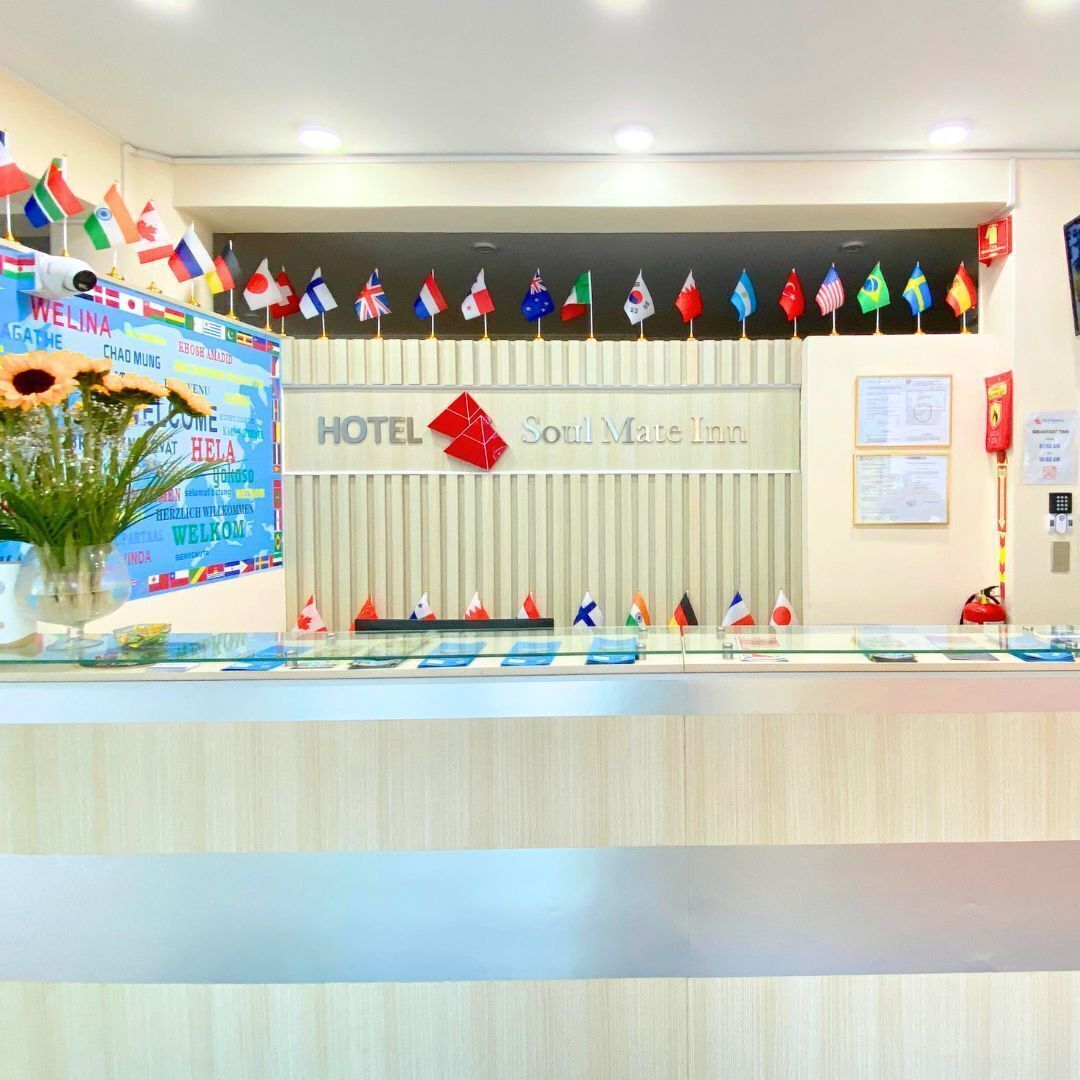 A hotel reception area with a sign reading "HOTEL Soul Mate Inn" and multiple national flags displayed above the reception desk.
