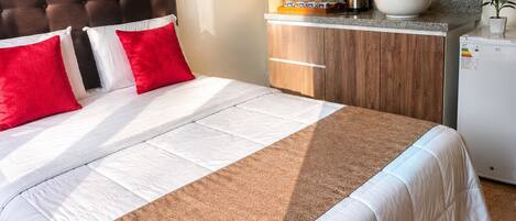 Una habitación de hotel con una cama, cabecero de madera, kitchenette con microondas, tetera y refrigerador.