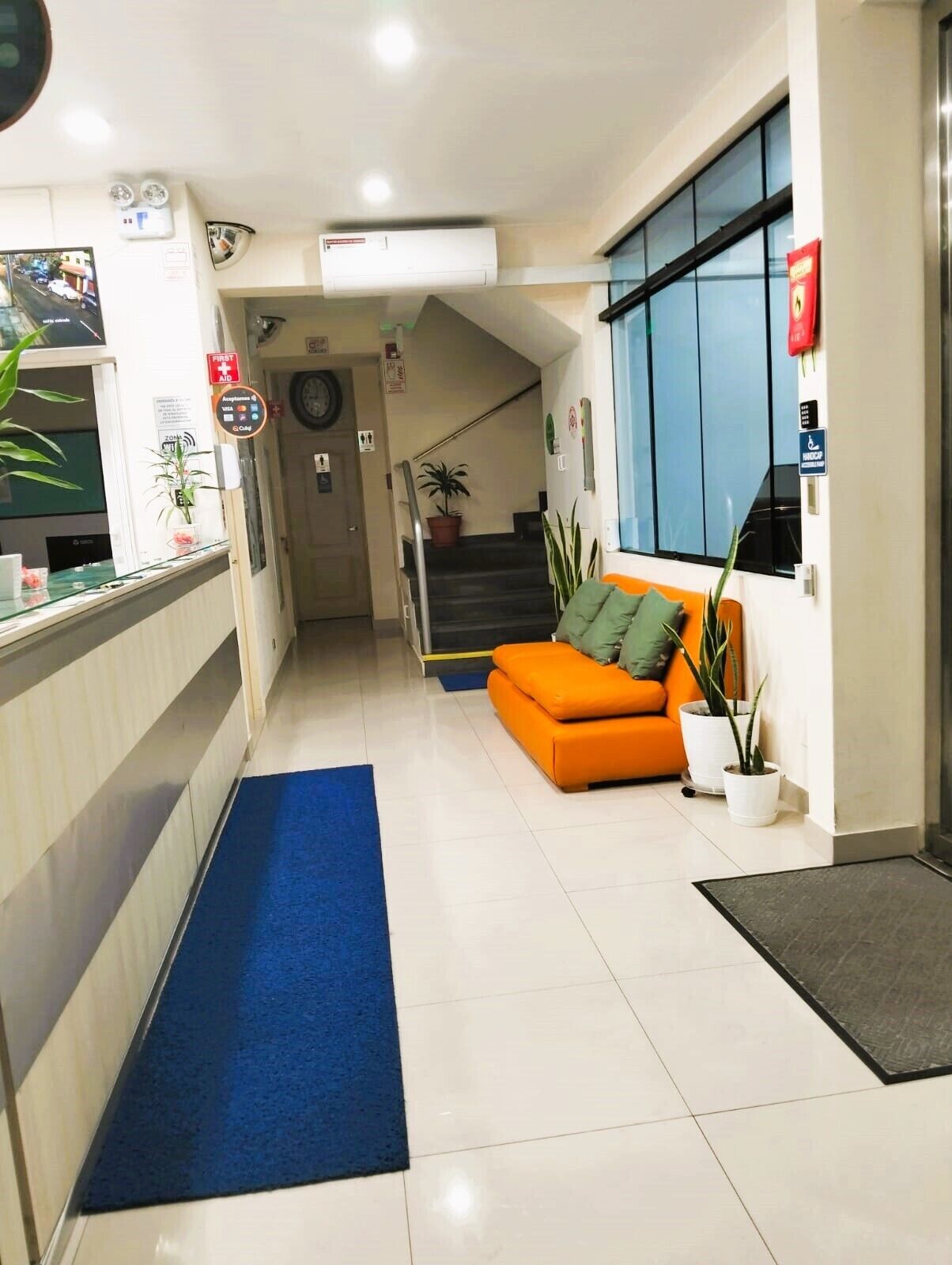 Un hall d’hôtel avec un comptoir d’accueil, une moquette bleue, un canapé orange et un escalier menant à un autre étage.
