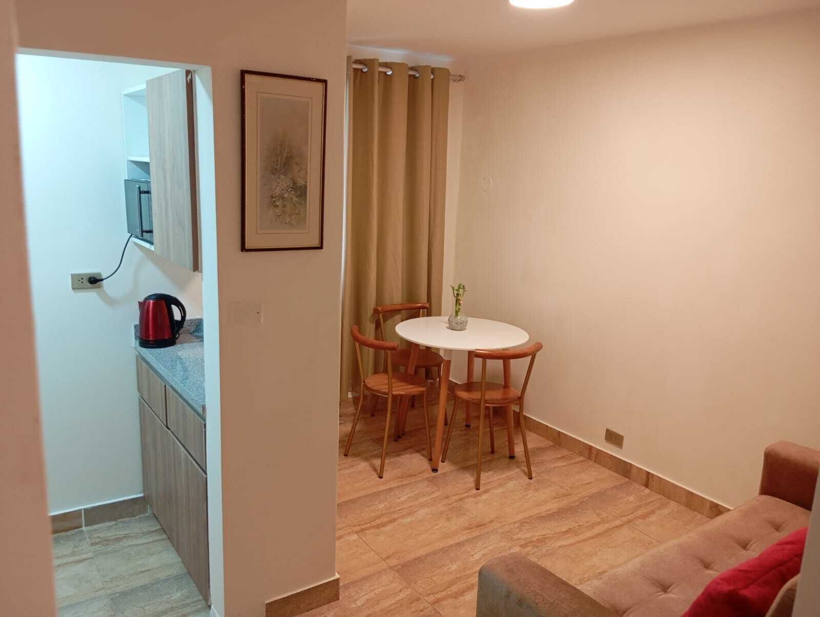 A compact living space with a kitchenette, a dining area with a table and four chairs, and a sofa.