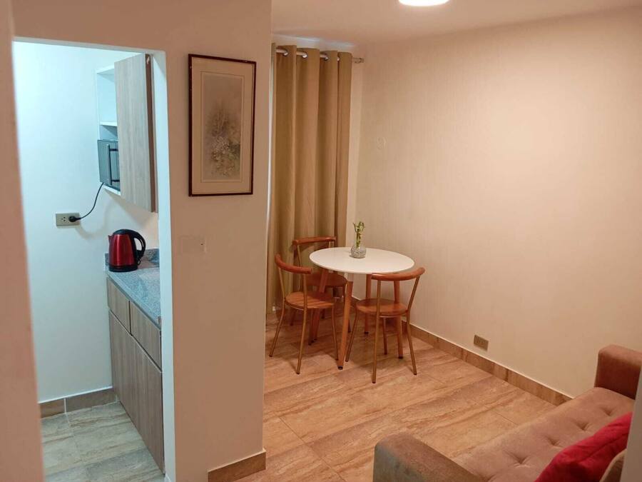 A compact living space with a kitchenette, a dining area with a table and four chairs, and a sofa.