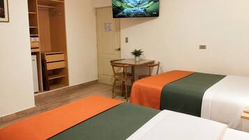 Habitación de hotel con dos camas, un escritorio con silla, televisor montado en la pared y un armario.