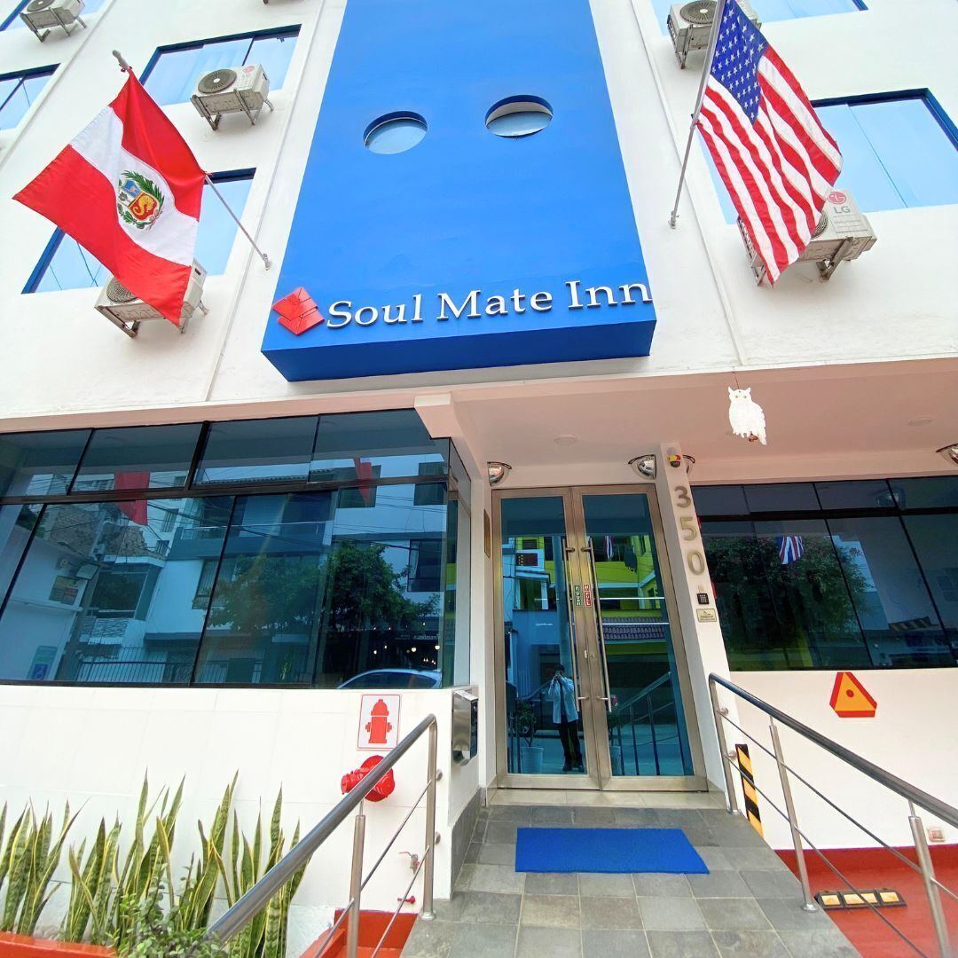 The exterior of the Soul Mate Inn, featuring a blue facade, a glass entrance, and flags of Peru and the USA.