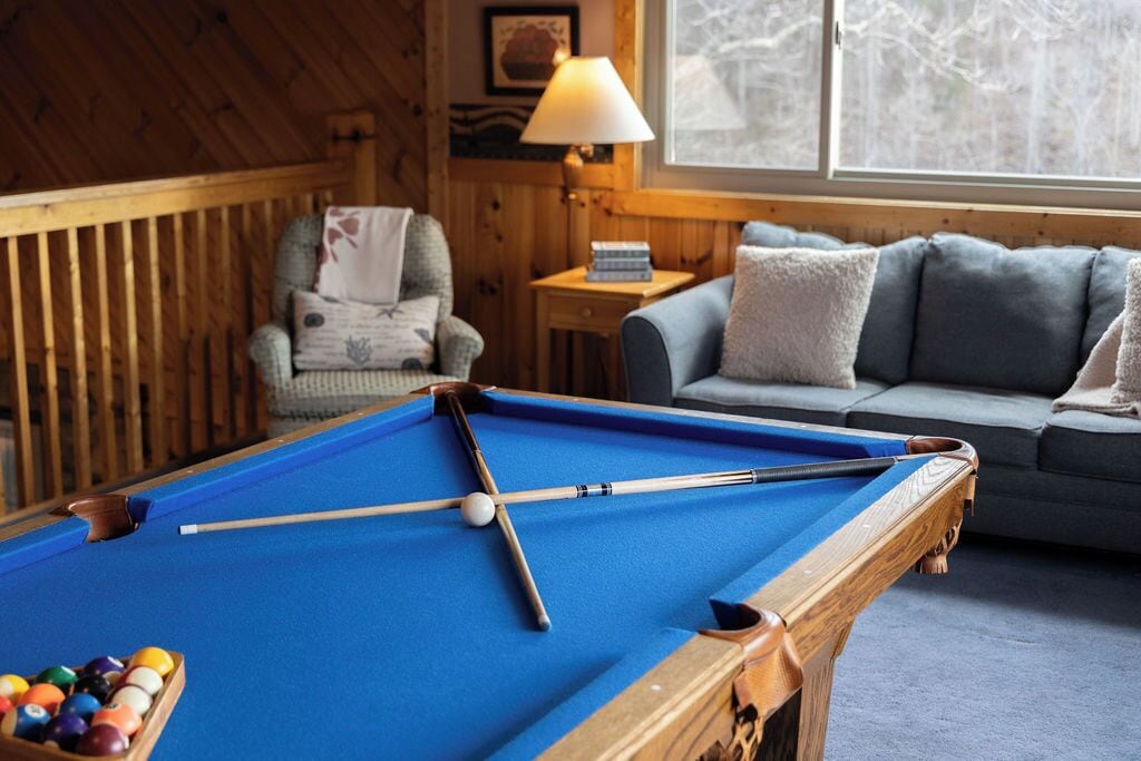 A pool table in a room with wooden walls, a sofa, and a lamp.