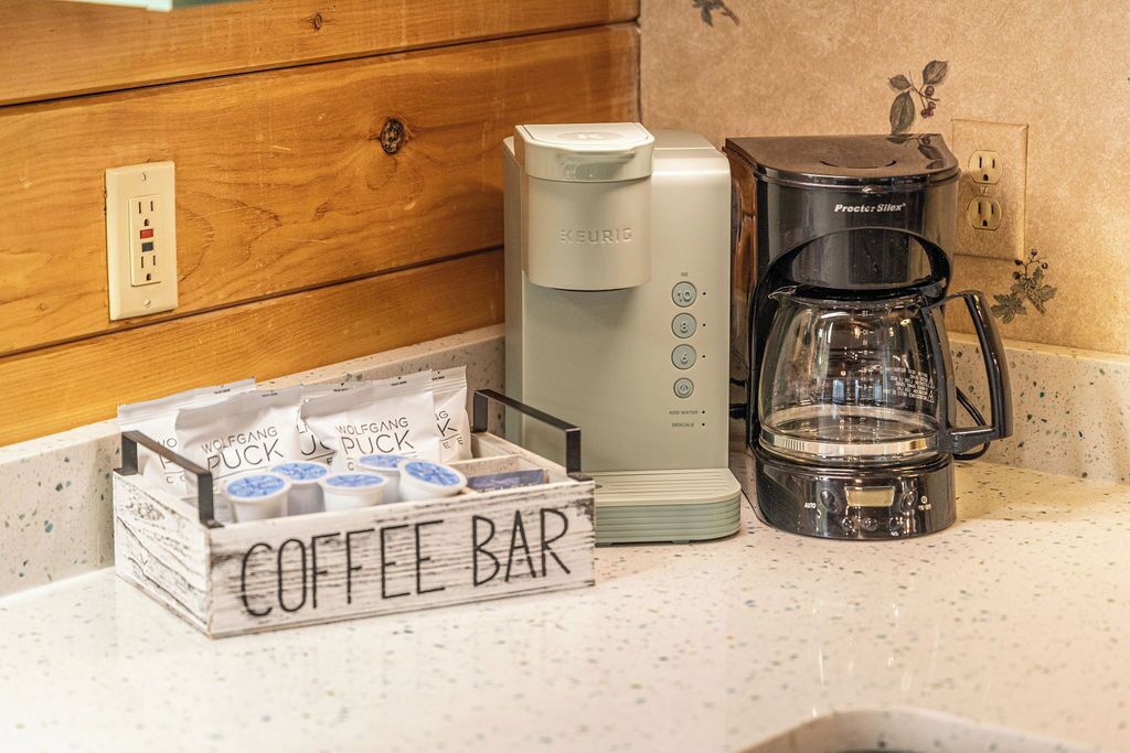 A kitchenette with a coffee maker, a Procter & Silvers coffee pot, and a coffee bar sign.