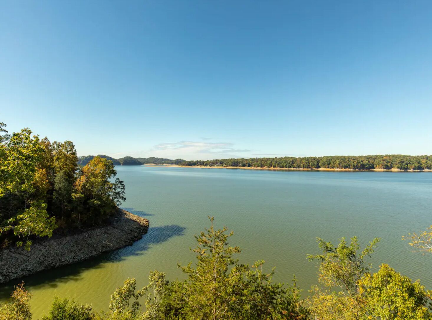 A large body of water surrounded by dense forest and a rocky shoreline.