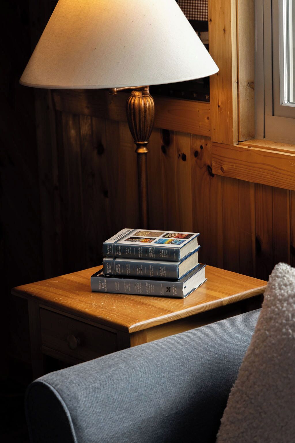 A wooden bedside table with a stack of books and a lamp.