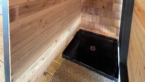 Interior de uma cabana de madeira com área de chuveiro, uma pequena janela e estrutura de porta de metal.