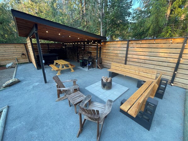 An outdoor patio area with wooden benches, a fire pit, and string lights. - Cozy cabin 1 mile to Sandy Ridge Bike Park, with RV hook up and EV charger. (Sandy)