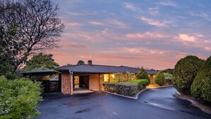 A single-story house with a brick exterior and a tiled roof, surrounded by well-maintained landscaping and a driveway.
