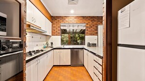 A modern kitchen with white cabinets, a brick accent wall, a built-in oven, and a dishwasher.