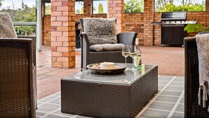 An outdoor patio area with wicker furniture, a grill, and a glass table with a bottle and glasses.