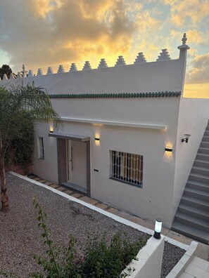 Um edifício moderno com telhado plano, entrada coberta e escadaria que leva ao andar superior.
