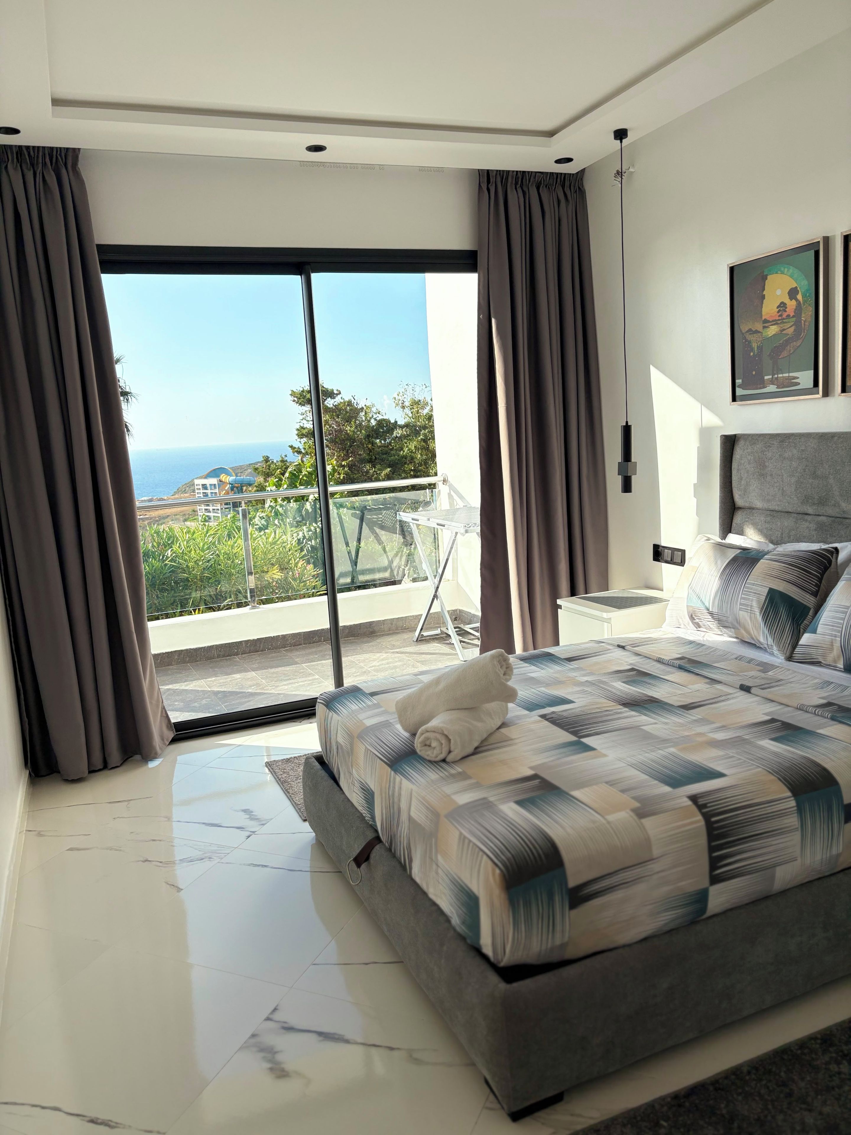 Quarto moderno com uma cama grande, varanda com vista para o mar e área de jantar com mesa e cadeiras.