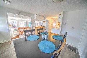 A modern kitchen with a dining area, featuring a black countertop, blue placemats, and a wooden dining table.