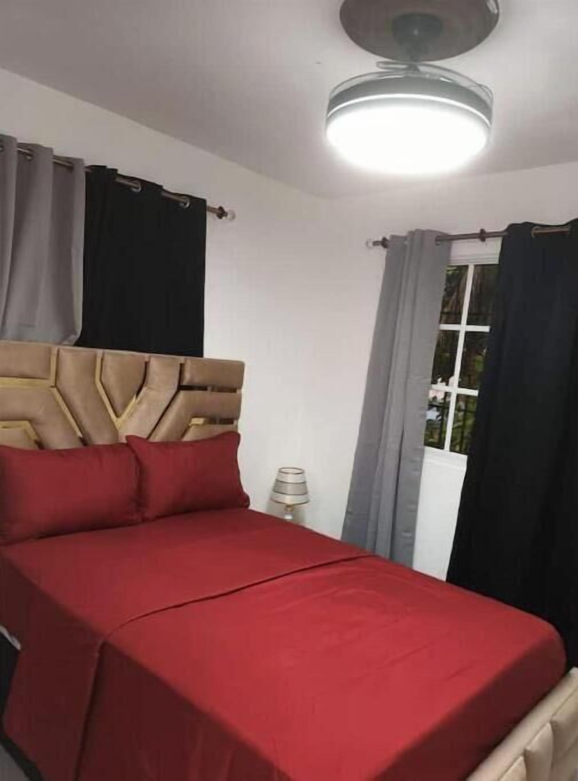 Una cama con cabecera, ropa de cama roja y una lámpara de noche.