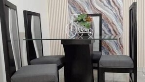 Een eethoek met een tafel met glazen blad, omringd door vier stoelen, een decoratief metalen bord met een fietsafbeelding en een wand met een marmerpatroon.