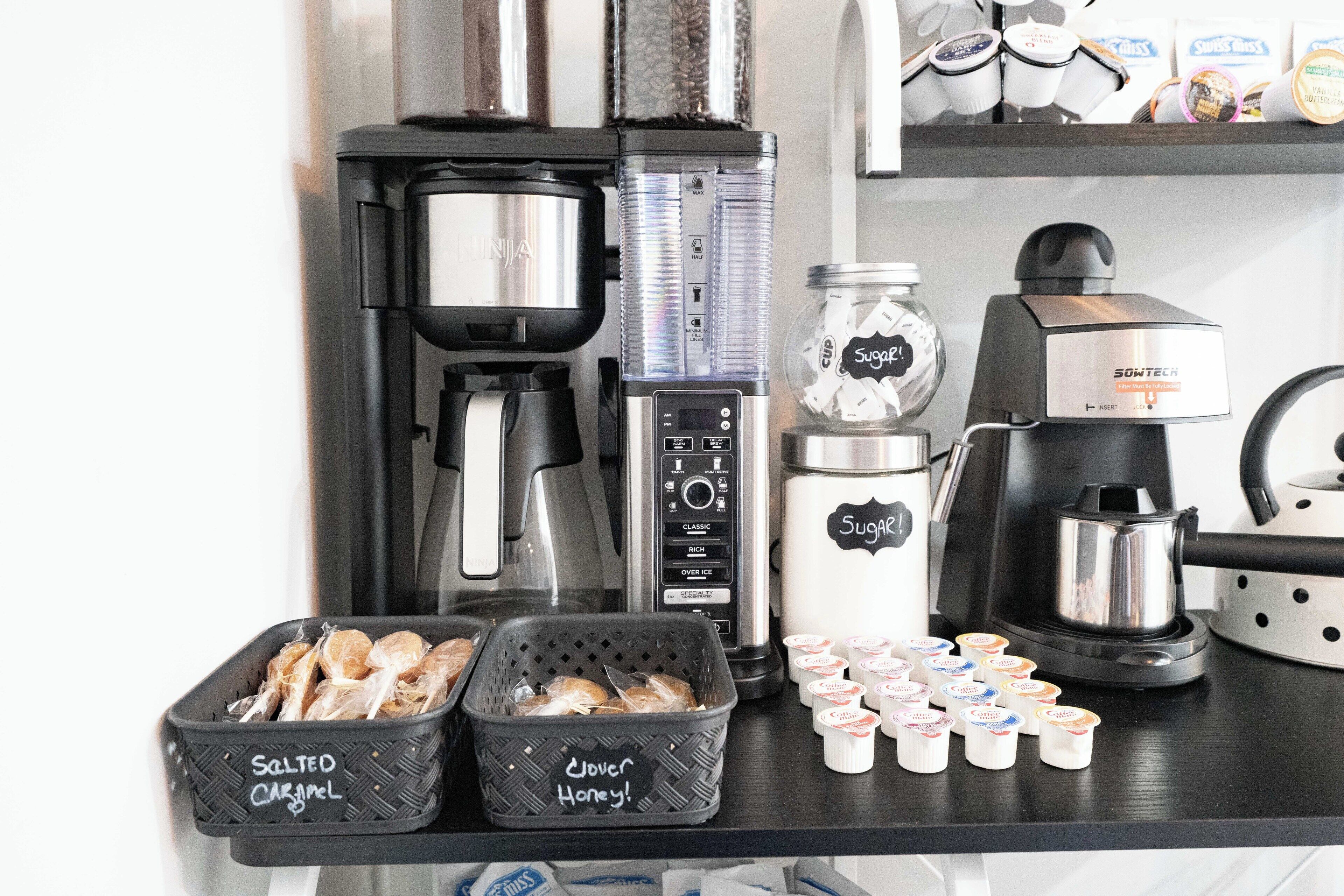 Un espace dédié au café, équipé de différents types de machines à café et de récipients étiquetés indiquant les différentes sortes de café et de sirops disponibles.