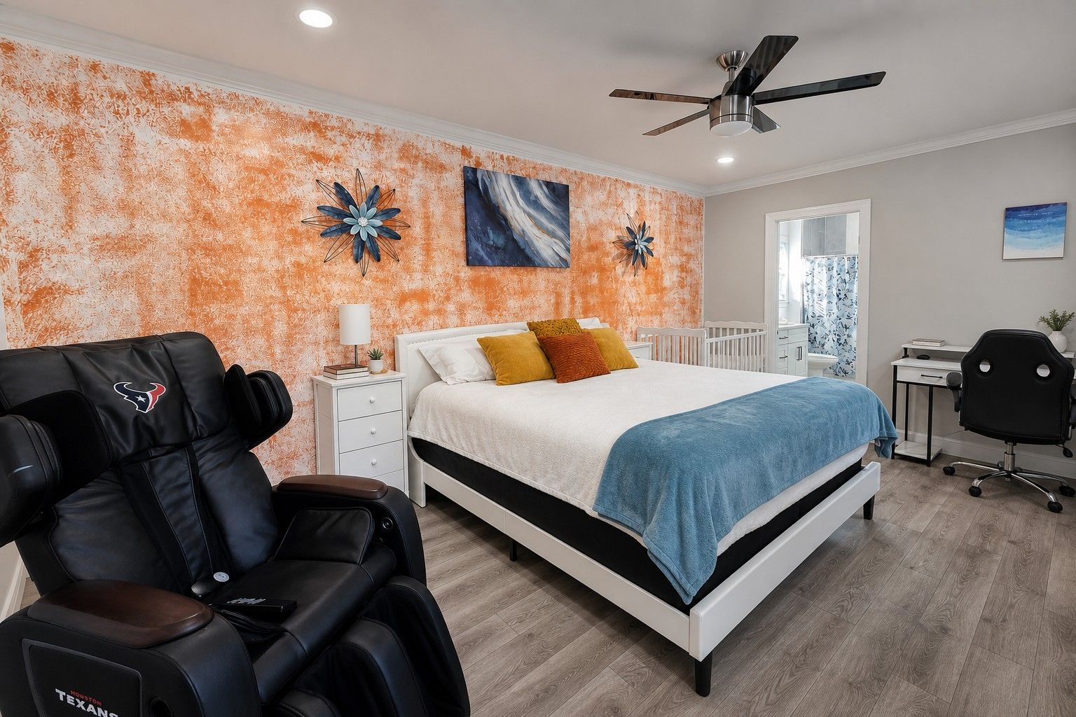 A bedroom with a bed, a desk, a chair, a massage chair, and a ceiling fan.