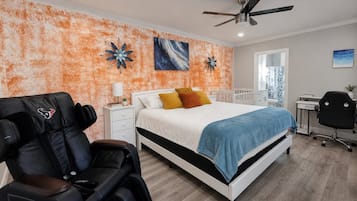A bedroom with a bed, a desk, a chair, a massage chair, and a ceiling fan.