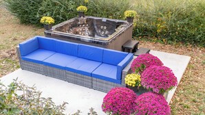 Un bain à remous doté d’un banc rembourré bleu, entouré de plantes en pot aux fleurs jaunes et roses.