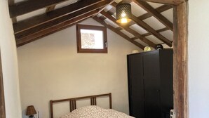Une chambre à coucher avec un lit en bois, une table de chevet avec une lampe, une armoire et une fenêtre laissant entrer la lumière naturelle.