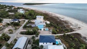 An aerial view of a coastal property with buildings, a beach, and a clear sky.