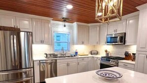 A modern kitchen with white cabinetry, stainless steel appliances, and a wooden ceiling.