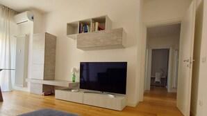 A modern living room with a flat-screen TV, built-in shelves, a radiator, and wooden flooring. - Family apartment in the center of Pisa - Design LM House (Pisa)