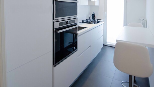 A modern kitchen with built-in appliances, a dining area with a white table and bar stool, and a large window providing natural light. - Family apartment in the center of Pisa - Design LM House (Pisa)