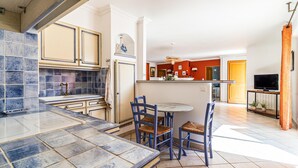 A modern kitchen with blue tiles, a dining area with blue chairs, and a TV in the living room. - 2 bedroom gorgeous home in Noves (Noves)
