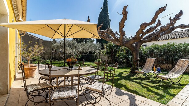 An outdoor patio with a round table and chairs, a large umbrella, and a decorative tree. - 2 bedroom gorgeous home in Noves (Noves)