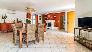 A dining area with wicker chairs and a wooden table, a fireplace, and a television on a wooden stand. - 2 bedroom gorgeous home in Noves (Noves)